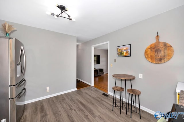 interior space with baseboards, wood finished floors, visible vents, and stainless steel fridge with ice dispenser