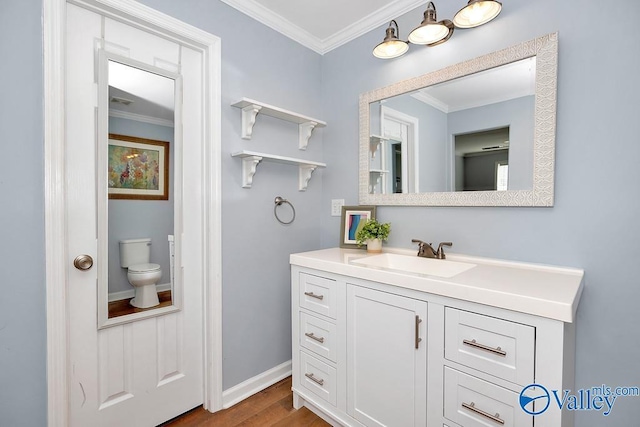 bathroom with toilet, wood finished floors, vanity, baseboards, and ornamental molding