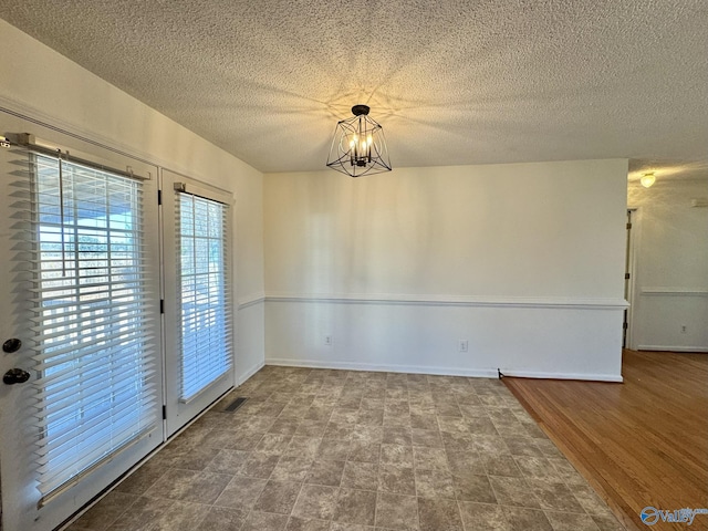 unfurnished room with wood-type flooring, an inviting chandelier, and a textured ceiling