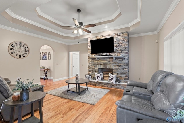 living room featuring a tray ceiling, a stone fireplace, ceiling fan, and hardwood / wood-style flooring