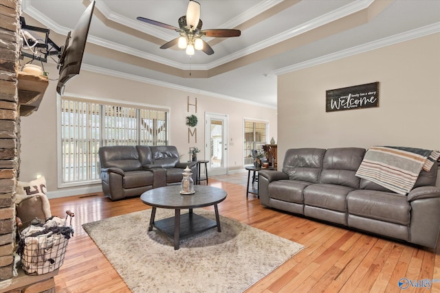 living room featuring hardwood / wood-style flooring, ceiling fan, ornamental molding, and a tray ceiling