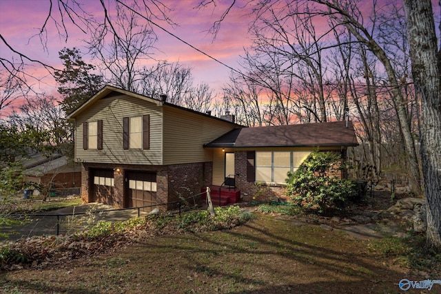 tri-level home featuring driveway, brick siding, a chimney, and an attached garage