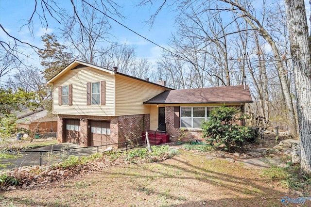 split level home featuring aphalt driveway, brick siding, a chimney, and an attached garage