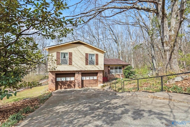 tri-level home with driveway, brick siding, an attached garage, and fence