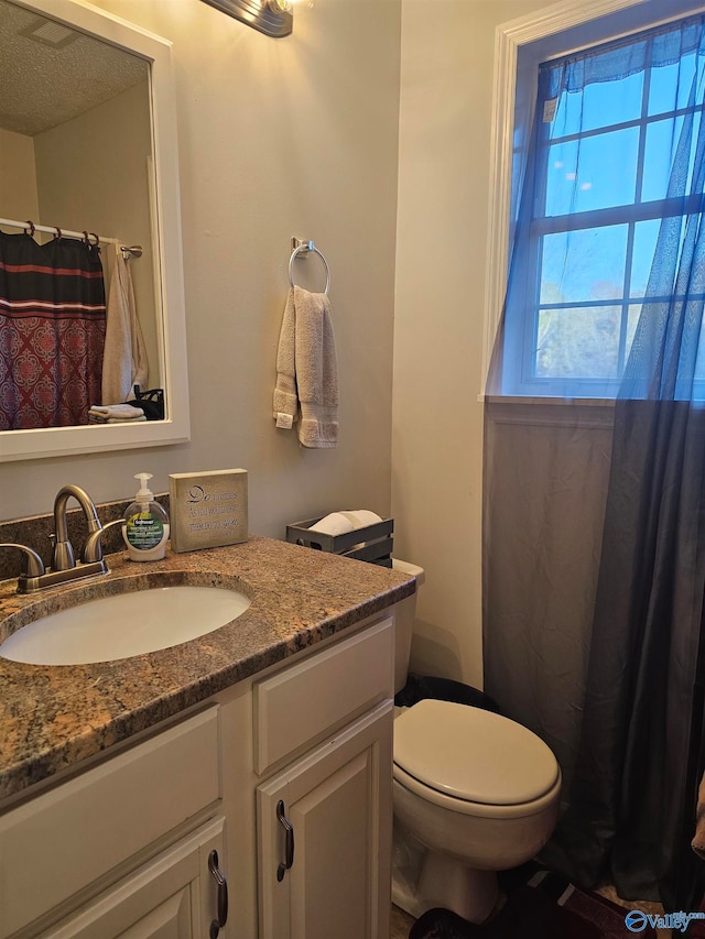 bathroom with a textured ceiling, vanity, and toilet