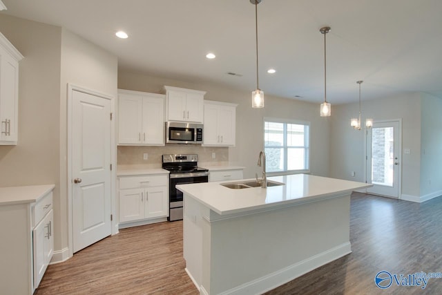 kitchen with stainless steel appliances, pendant lighting, white cabinets, and an island with sink