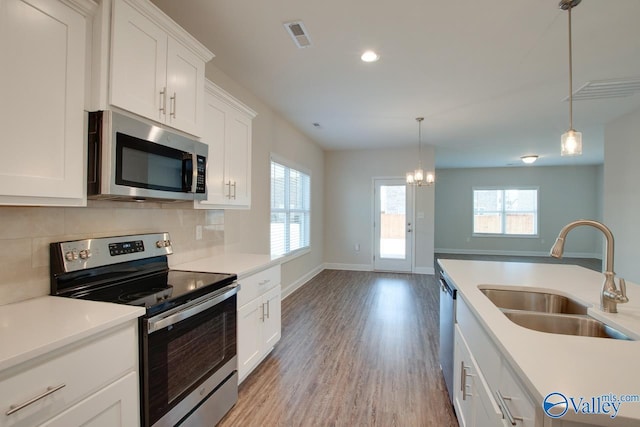 kitchen with white cabinetry, stainless steel appliances, plenty of natural light, sink, and hanging light fixtures