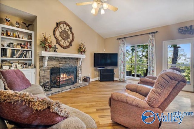 living room featuring ceiling fan, built in features, light hardwood / wood-style floors, lofted ceiling, and a stone fireplace