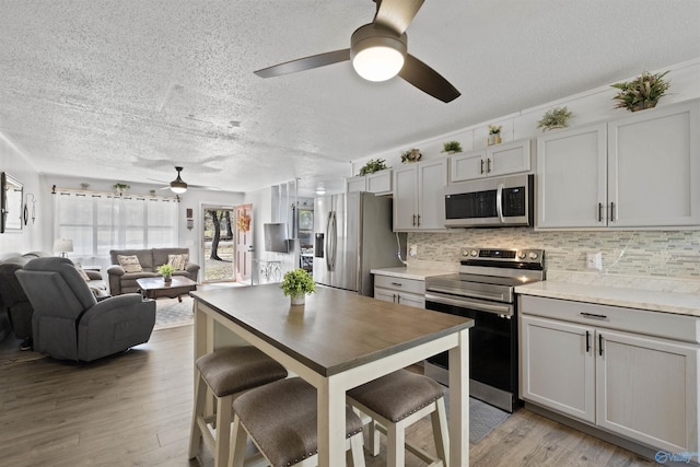 kitchen featuring light wood-type flooring, backsplash, a breakfast bar, stainless steel appliances, and gray cabinets