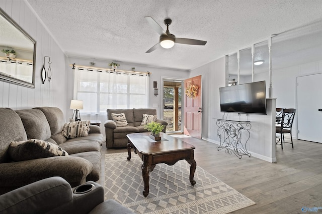 living room with wood walls, ceiling fan, light hardwood / wood-style floors, and a textured ceiling