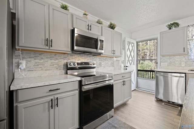 kitchen with tasteful backsplash, gray cabinetry, a textured ceiling, stainless steel appliances, and light hardwood / wood-style flooring