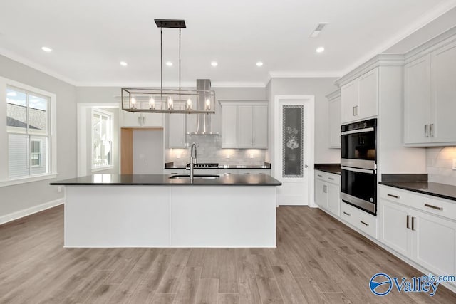 kitchen featuring sink, hanging light fixtures, double oven, an island with sink, and white cabinets