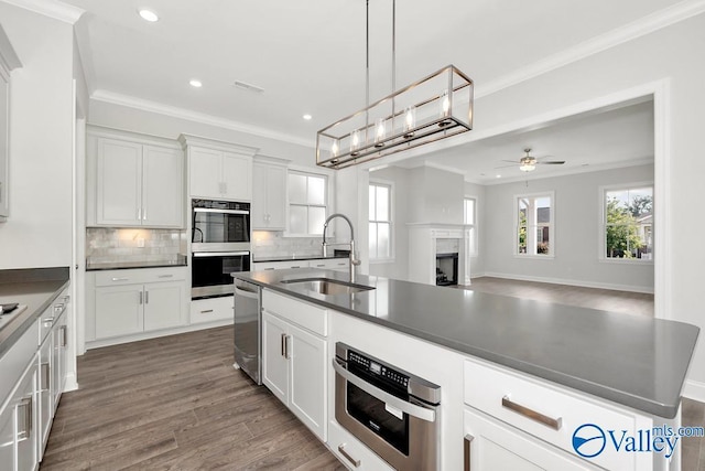 kitchen featuring ornamental molding, an island with sink, sink, and white cabinets