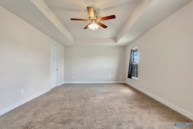 empty room with light carpet, ceiling fan, and a raised ceiling