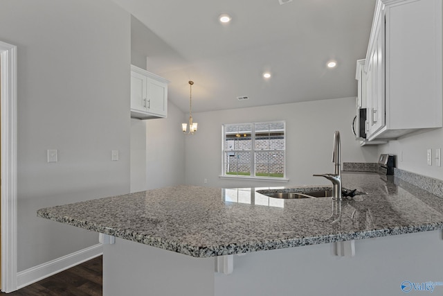 kitchen with stone countertops, white cabinets, a breakfast bar, a peninsula, and a sink