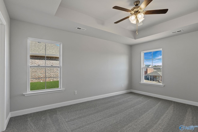 spare room featuring a tray ceiling, visible vents, plenty of natural light, and baseboards