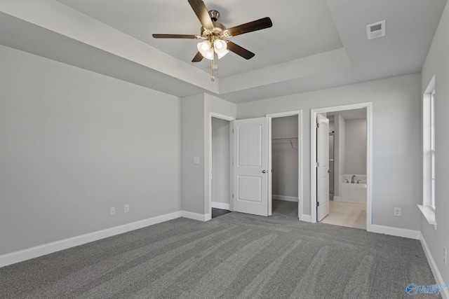 unfurnished bedroom with ensuite bathroom, carpet flooring, visible vents, baseboards, and a tray ceiling