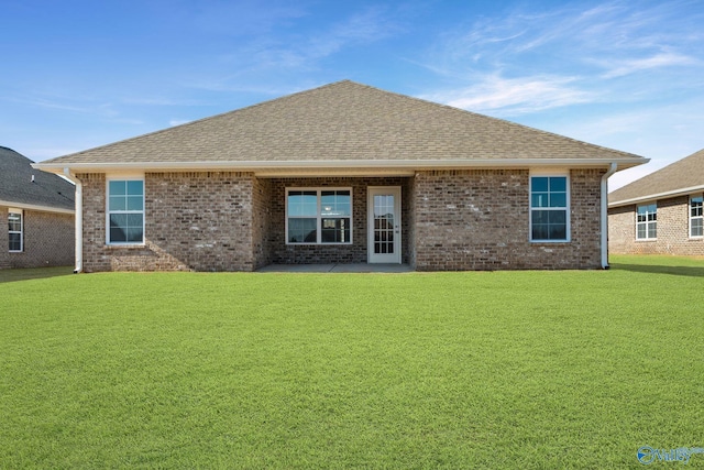 rear view of house featuring brick siding, a lawn, and roof with shingles