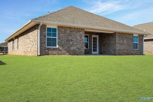 rear view of property featuring a shingled roof, a lawn, and brick siding