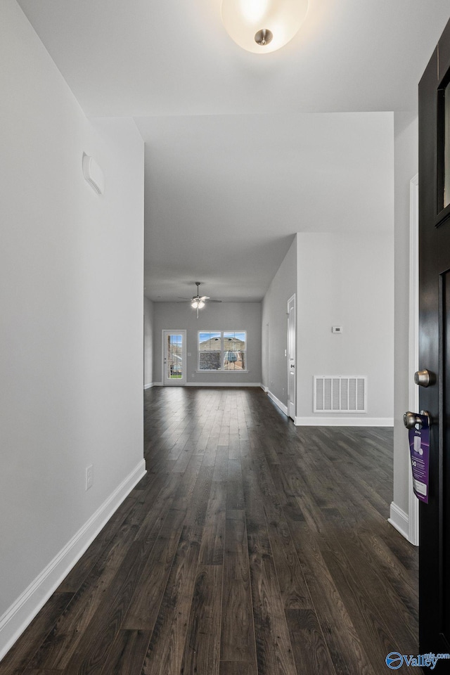 unfurnished living room featuring dark wood-type flooring, a ceiling fan, visible vents, and baseboards