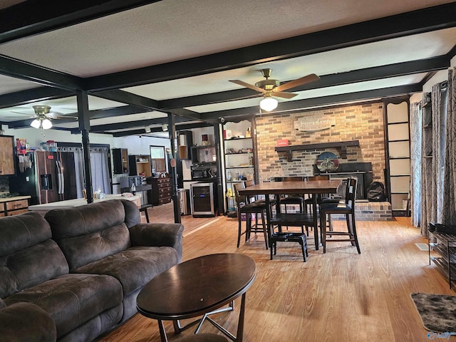 living room featuring beamed ceiling, ceiling fan, light wood-type flooring, and a textured ceiling