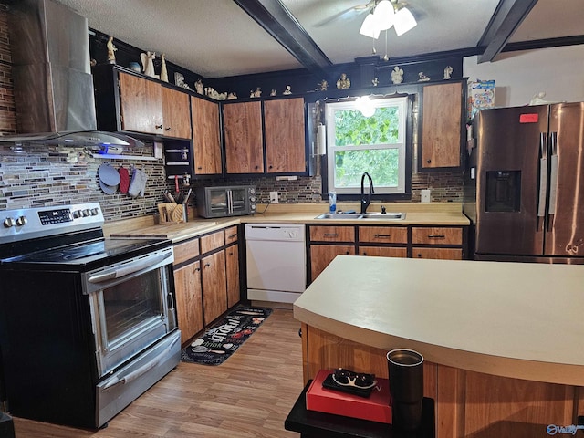 kitchen featuring sink, light wood-type flooring, appliances with stainless steel finishes, beamed ceiling, and wall chimney range hood