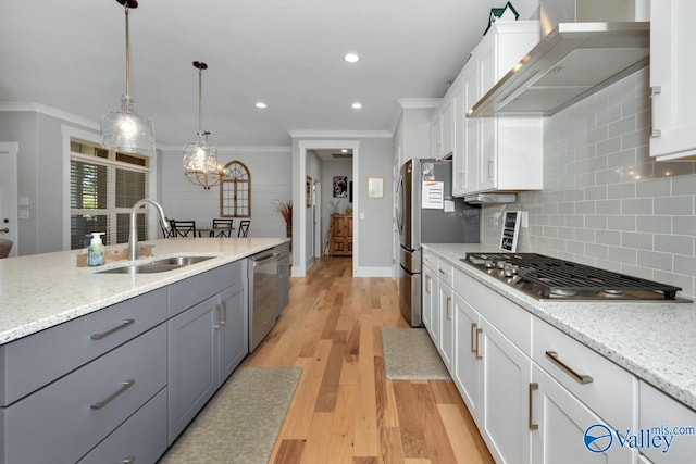 kitchen with light wood-type flooring, stainless steel appliances, sink, wall chimney range hood, and white cabinets