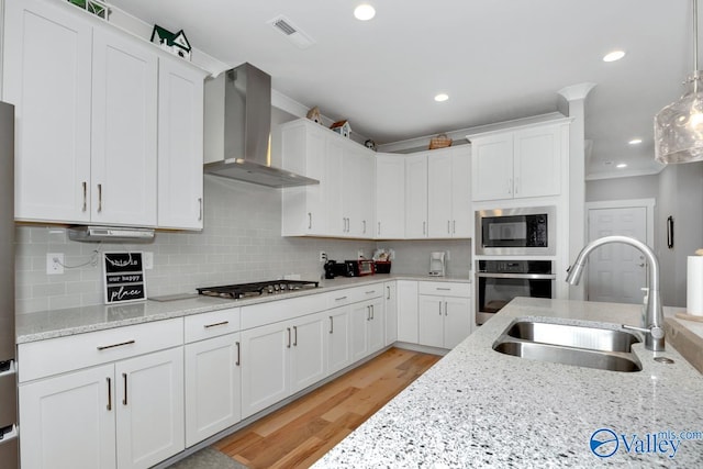 kitchen featuring wall chimney range hood, sink, light wood-type flooring, white cabinetry, and stainless steel appliances