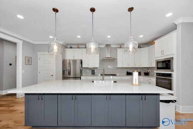 kitchen with appliances with stainless steel finishes, white cabinetry, a large island with sink, and wall chimney exhaust hood