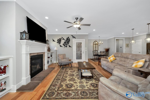 living room featuring ceiling fan with notable chandelier, light hardwood / wood-style floors, crown molding, and a tiled fireplace