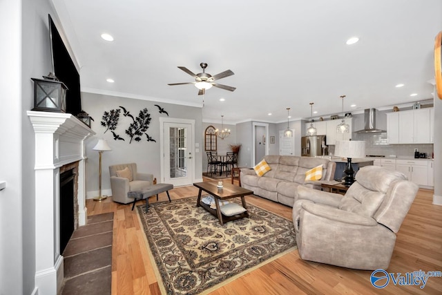 living room with ceiling fan with notable chandelier, light wood-type flooring, and crown molding