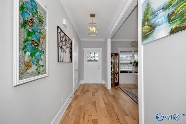 doorway to outside with light hardwood / wood-style floors, ornamental molding, and a notable chandelier