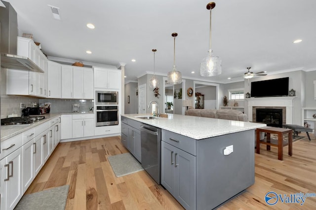 kitchen with a kitchen island with sink, wall chimney range hood, gray cabinets, appliances with stainless steel finishes, and white cabinetry