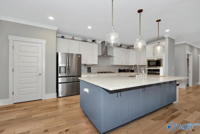 kitchen with appliances with stainless steel finishes, wall chimney range hood, a large island with sink, white cabinets, and light hardwood / wood-style floors