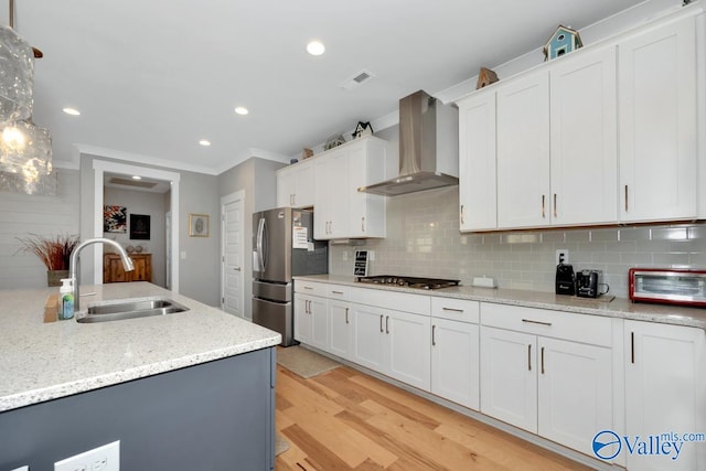 kitchen with white cabinets, wall chimney range hood, sink, light wood-type flooring, and stainless steel appliances