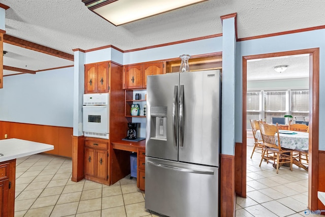 kitchen with light tile patterned floors, brown cabinetry, stainless steel refrigerator with ice dispenser, wainscoting, and white oven