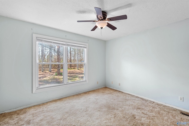 empty room with visible vents, a textured ceiling, carpet flooring, and a ceiling fan
