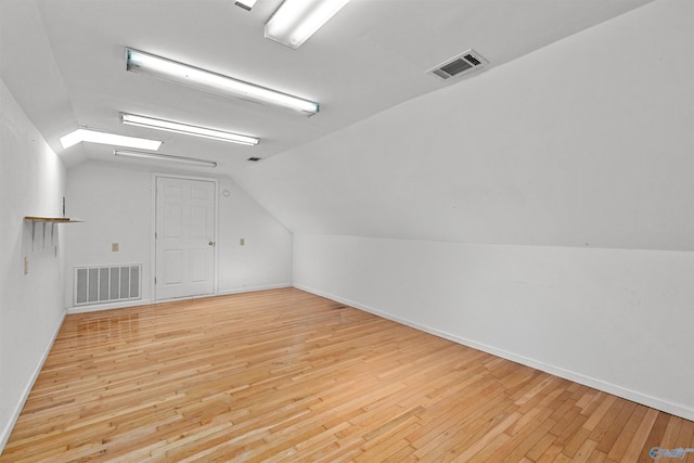 additional living space with lofted ceiling with skylight, visible vents, and wood-type flooring
