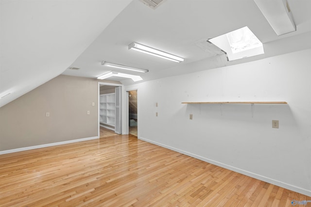 additional living space featuring vaulted ceiling with skylight, baseboards, and light wood finished floors