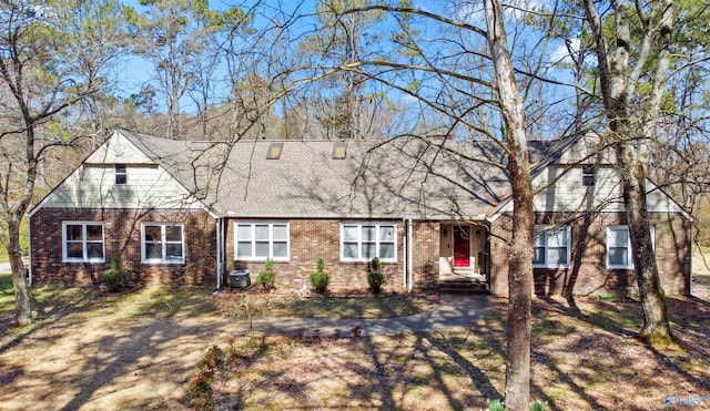 view of front of property with central air condition unit, brick siding, and roof with shingles
