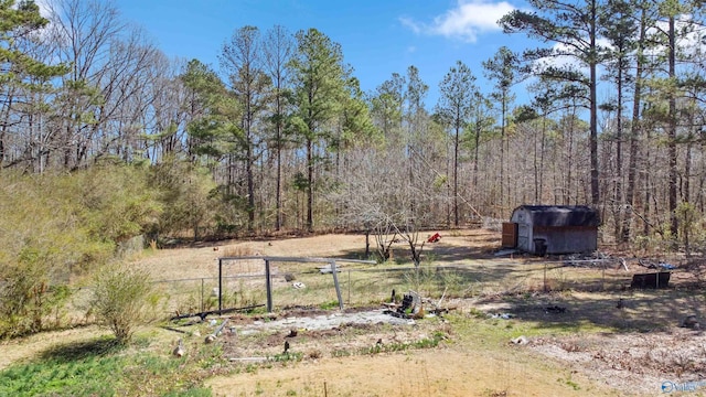 view of yard featuring an outdoor structure, fence, a forest view, and a shed