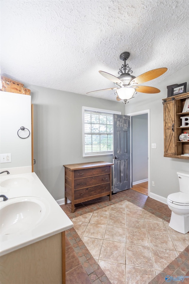 bathroom with ceiling fan, vanity, a textured ceiling, tile patterned floors, and toilet