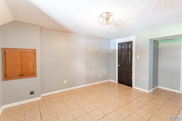 tiled spare room featuring lofted ceiling and a textured ceiling