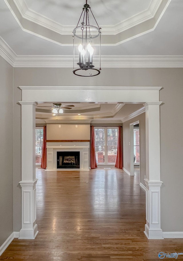 unfurnished living room featuring ornamental molding, a raised ceiling, and decorative columns