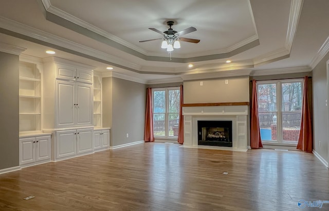 unfurnished living room with a raised ceiling, ceiling fan, and plenty of natural light