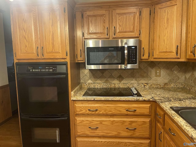 kitchen featuring black appliances, decorative backsplash, and light stone countertops