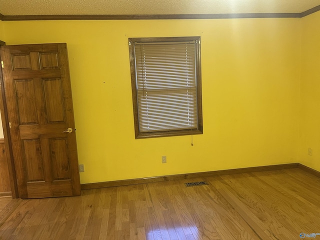 unfurnished room with a textured ceiling, light wood-type flooring, and crown molding