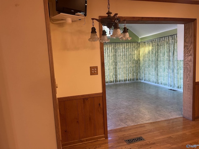 unfurnished dining area featuring hardwood / wood-style flooring, a notable chandelier, and wood walls