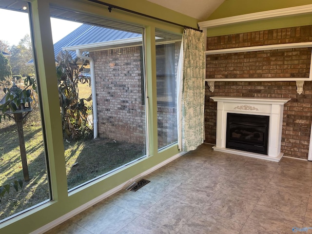 unfurnished living room featuring a fireplace, tile patterned flooring, vaulted ceiling, and a healthy amount of sunlight