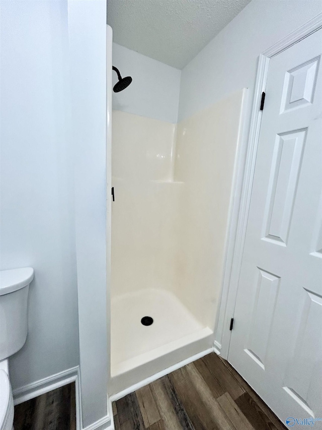 bathroom featuring toilet, wood-type flooring, walk in shower, and a textured ceiling